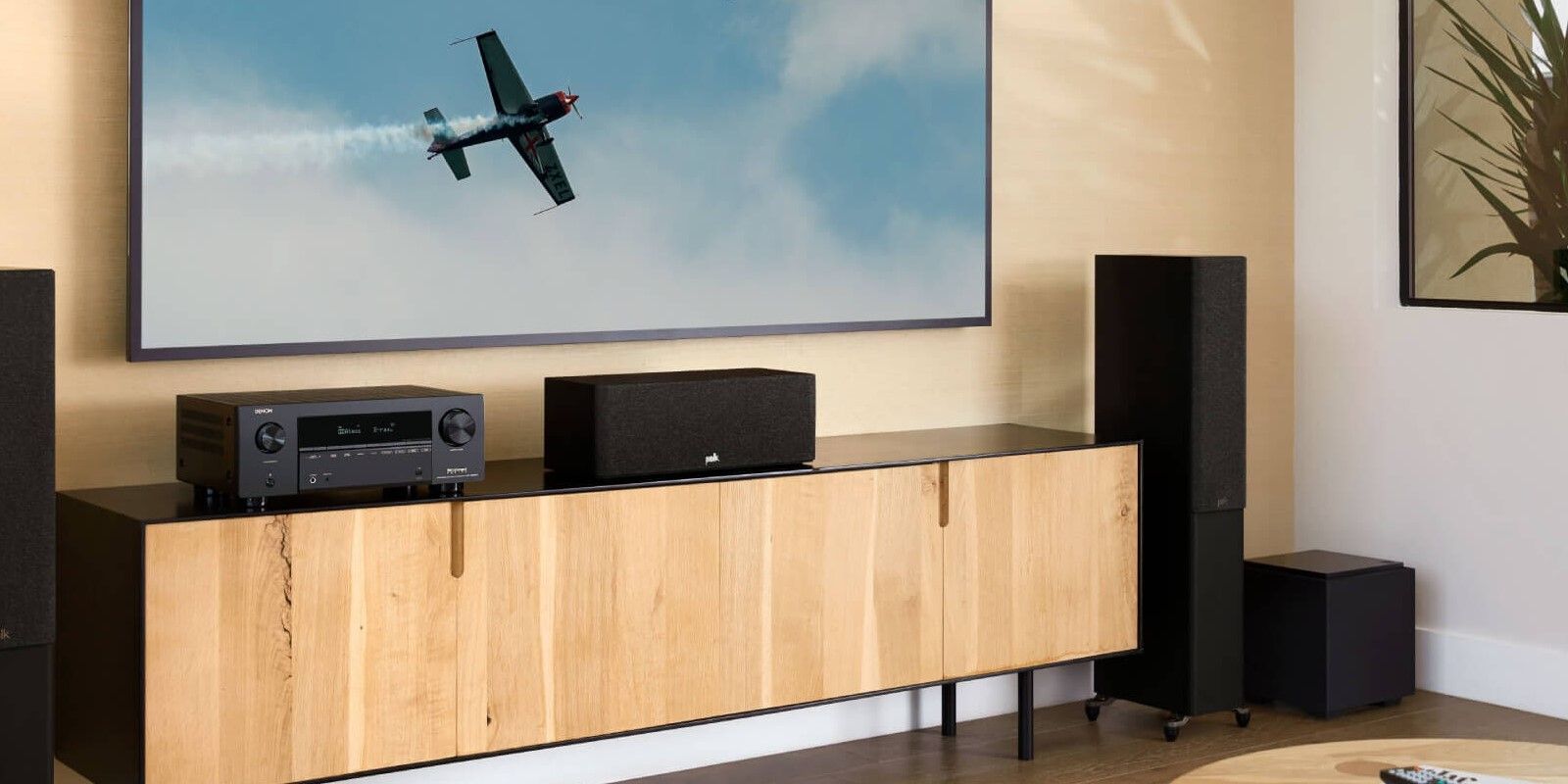 List Image of the Denon AVR-X2000H AV Amplifier in a Hi-Fi system setup in a living room on a wooden cabinet below a widescreen TV 