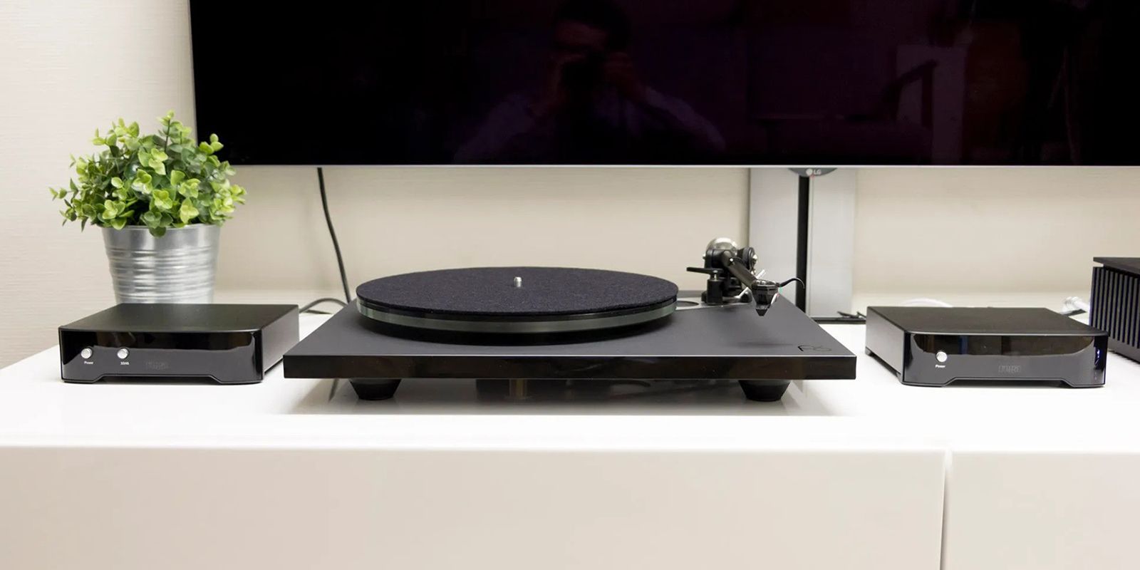 Rega planar 6 turntable on a white table surrounded by Hi-Fi accessories and wall-mounted tv