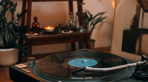 A blue and black vinyl being played on a turntable, in a room full of plants and candlelight, to showcase an ideal setup with speakers for turntables.